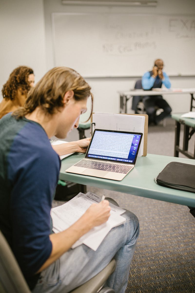 Travels Air touch College student focused on exam preparation in a classroom setting, using a laptop and notes.